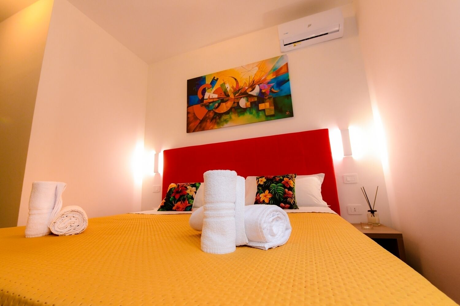 Una habitación de hotel con una colcha amarilla, un cabecero rojo y un cuadro sobre la cama.