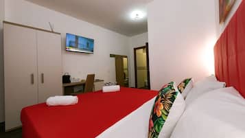 Ein Hotelzimmer mit roter Bettdecke, weißen Kissen, einem Fernseher, einem Schreibtisch und einem Schild für eine Kaffeebar.