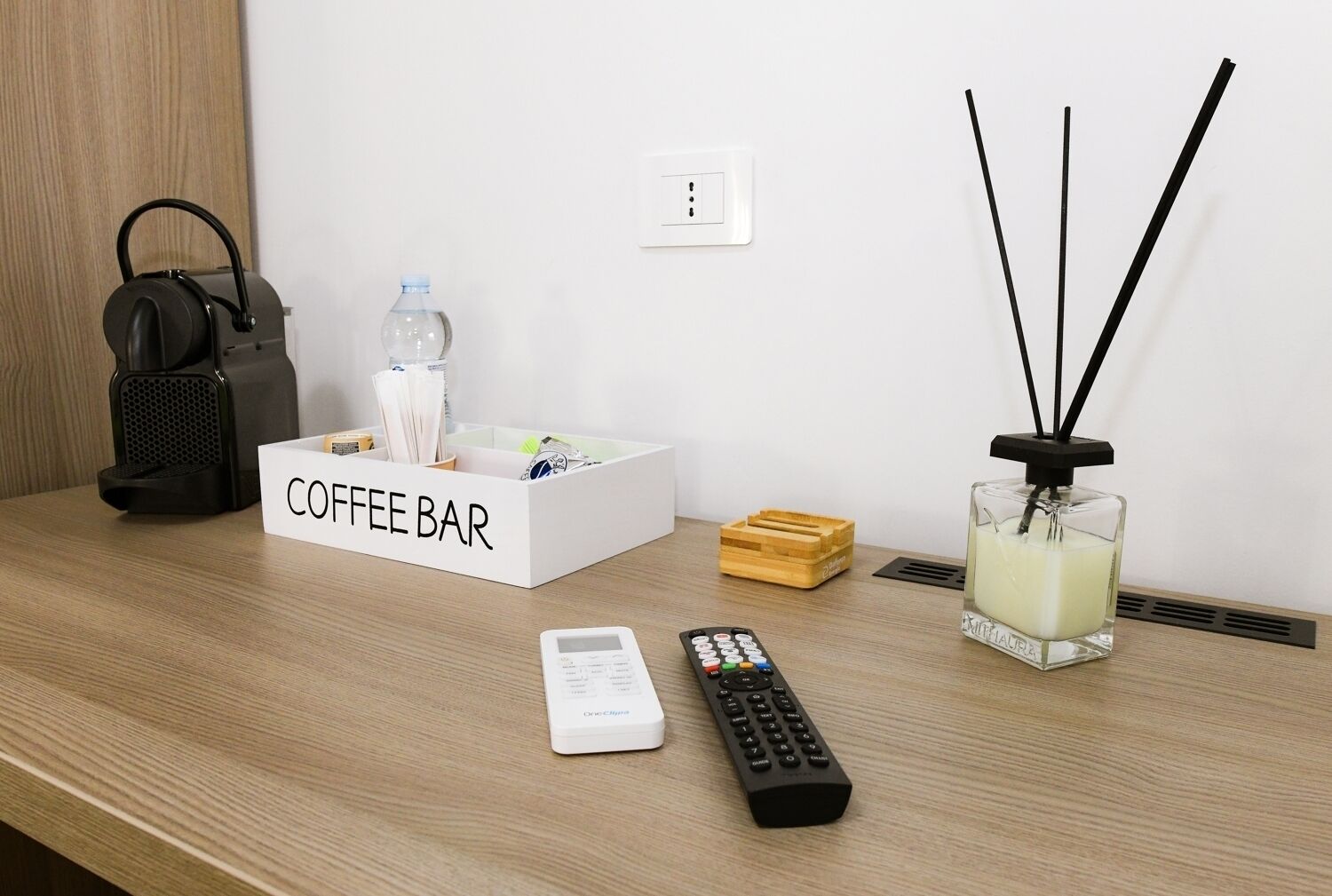 Un coin café aménagé avec une bouteille d’eau, une télécommande et une bougie parfumée sur une table en bois.
