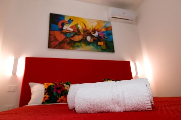 A hotel room with a red headboard, a colorful abstract painting, and a white towel on the bed. - 100 Passi dal Porto (Civitavecchia)