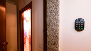 Entrada a una habitación de hotel con puerta, un portero automático en la pared y una vista de la habitación con cama y cortinas.