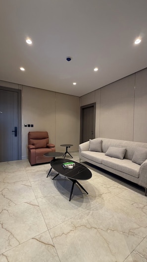 Ein modernes Wohnzimmer mit Sofa, Sessel, Couchtisch, deckenmontierten Leuchten und einer Tür.