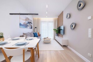 Un salon moderne comprenant un coin repas, un téléviseur à écran plat fixé au mur et une grande fenêtre avec des rideaux.