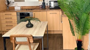 Una cocina moderna con armarios de madera, una mesa de comedor con sillas, un microondas y una planta grande en maceta.