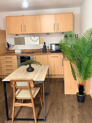Eine moderne Küche mit Holzschränken, einem Esstisch mit Stühlen, einer Mikrowelle und einer großen Topfpflanze.
