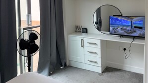 Habitación de hotel con cama, escritorio con televisor, ventilador y ventana con cortinas.