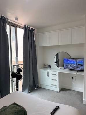 Ein Hotelzimmer mit Bett, Schreibtisch mit Fernseher, Ventilator und einem Fenster mit Vorhängen.