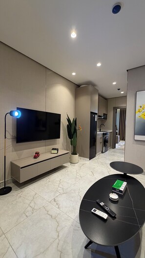 Ein modernes Wohnzimmer mit Flachbildfernseher, einer Zimmerpflanze, einem Couchtisch und einer Küchenzeile im Hintergrund.