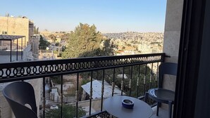 Varanda com duas cadeiras e uma mesa, com vista para uma paisagem urbana com edifícios e árvores.