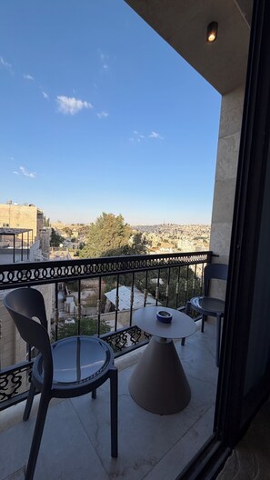 Ein Balkon mit zwei Stühlen und einem Tisch, der auf einen Stadtblick mit Gebäuden und Bäumen blickt.