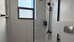 Et moderne badeværelse med brusekabine i glas, toilet og et vindue.