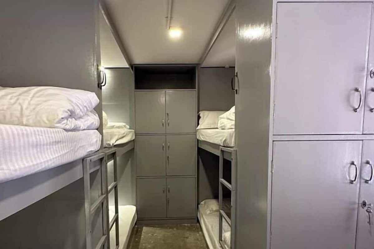 Una habitación estrecha con literas, un armario y una ventana pequeña.