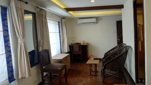 Une pièce avec un plancher en bois, un bureau, une chaise, une petite table, un fauteuil en osier et une fenêtre avec des rideaux.