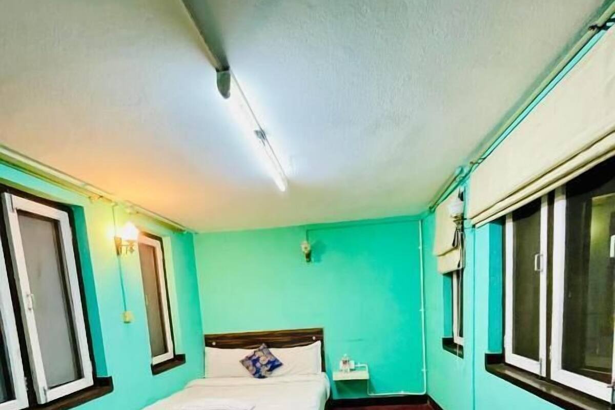 Una habitación pequeña con cama individual, paredes color aguamarina, alfombra roja y una ventana en una pared.