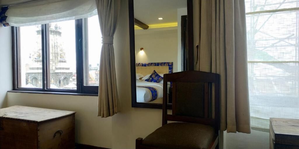 Ein Hotelzimmer mit Bett, einem Sessel, einem kleinen Tisch und einem Fenster mit Vorhängen.