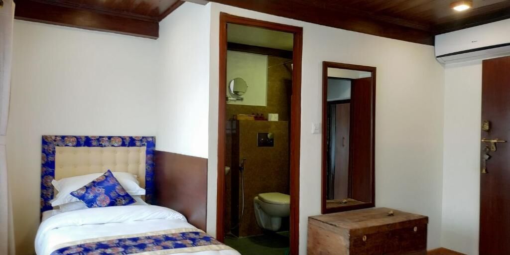 A bedroom with a bed, a wooden nightstand, a bathroom with a toilet, and a mirror.
