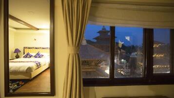 A hotel room with a bed, a nightstand, a lamp, and a view of a pagoda through a window.