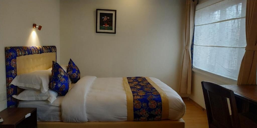 A bed with a headboard, pillows, a blanket, a bedside table, a chair, a window with curtains, and a framed picture on the wall.