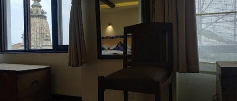 Una habitación con cama, una silla, ventana con cortinas, un espejo y vista a un edificio.