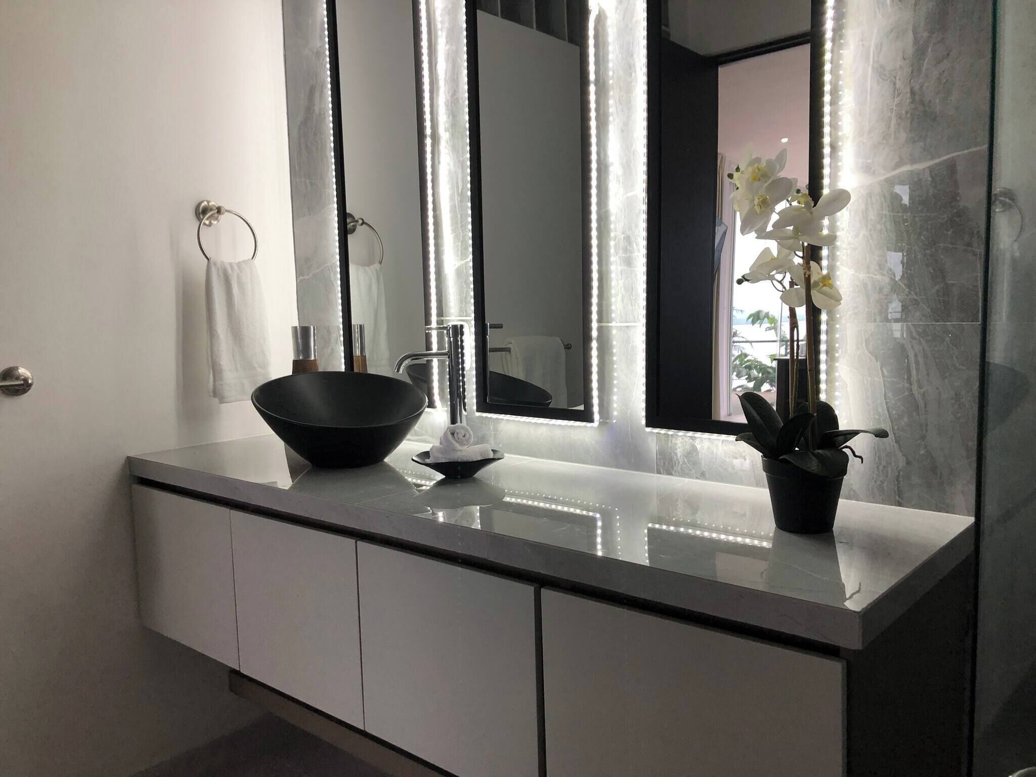 A modern bathroom with a large mirror, a black bowl sink, and a potted orchid.