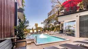 Ein Pool auf dem Dach mit Liegestühlen, einer Holzbank und einem roten Sonnenschirm.