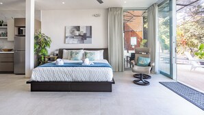 Ein modernes Schlafzimmer mit Bett, Deckenventilator, Blick ins Freie und einer Küche im Hintergrund.