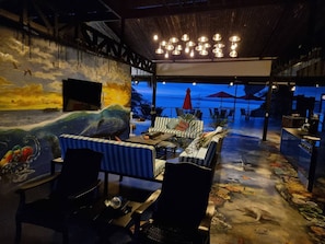 An outdoor dining area with striped furniture, a mural of ocean life, and a view of the sea. - Penthouse with Panoramic Ocean Views - Hotel VOS (Manuel Antonio)