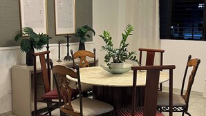 A dining area with a round table, six chairs, a chandelier, two potted plants, and framed certificates on the wall. - The Distrito Atelier (Santo Domingo)