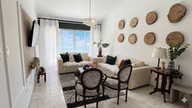 A living room with a sofa, chairs, a coffee table, a TV, and decorative wall art. - The Distrito Atelier (Santo Domingo)