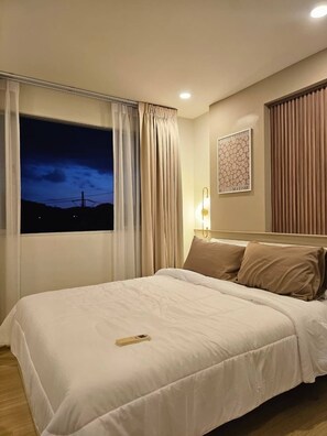 Ein Hotelzimmer mit Bett, Vorhängen, Blick auf den Nachthimmel, einer Wandleuchte und einem gerahmten Kunstwerk.