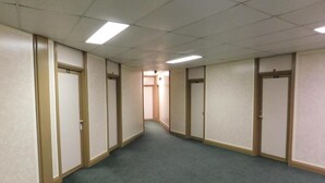 Un pasillo con puertas a ambos lados, suelo alfombrado e iluminación fluorescente.