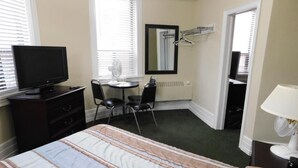 Habitación de hotel con cama, televisión, una mesita con sillas, espejo y ventana con persianas.