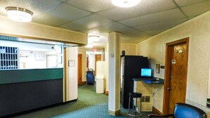 Un vestíbulo de hotel con mostrador de recepción, refrigerador, computadora, una silla y una mesita.