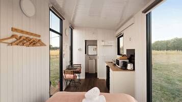 Una habitación moderna con cama, perchero de madera, pequeña cocina y vistas al exterior.