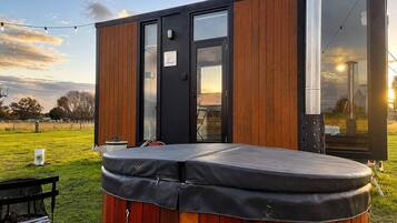 A modern outdoor hot tub with a wooden exterior, a glass door, and a string of lights.