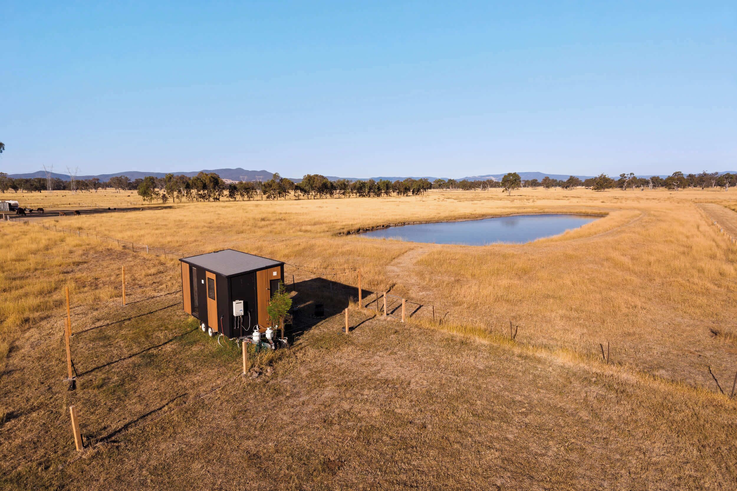 A small, isolated building with a fenced area and a pond nearby.