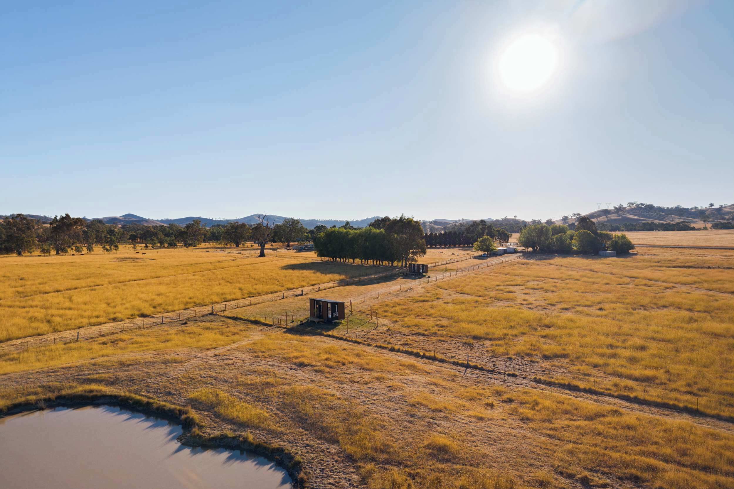 Paisagem rural com um campo cercado, um pequeno edifício e um corpo d'água.