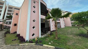 A pink building with a central entrance, surrounded by a grassy area and a palm tree. - Charming 2-bedroom apartment with AC in Mombasa (Mombasa)