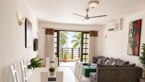 A modern living room with a dining area, a ceiling fan, and a view of palm trees. - Charming 2-bedroom apartment with AC in Mombasa (Mombasa)