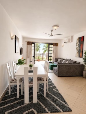 Un salon moderne avec un coin repas, un ventilateur de plafond et une vue sur des palmiers.