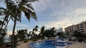A pool area with lounge chairs, palm trees, and a building in the background. - Charming 2-bedroom apartment with AC in Mombasa (Mombasa)