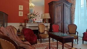 Quarto com um espelho grande, um armário de madeira, uma poltrona vermelha, um tapete estampado e uma mesa com cadeiras.