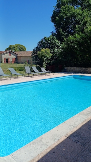 Ein klares, blaues Schwimmbecken mit Liegestühlen und einer Steinmauer.