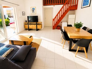 Ein modernes Wohnzimmer mit Sofa, Fernseher, Esstisch, Stühlen und einer Treppe.
