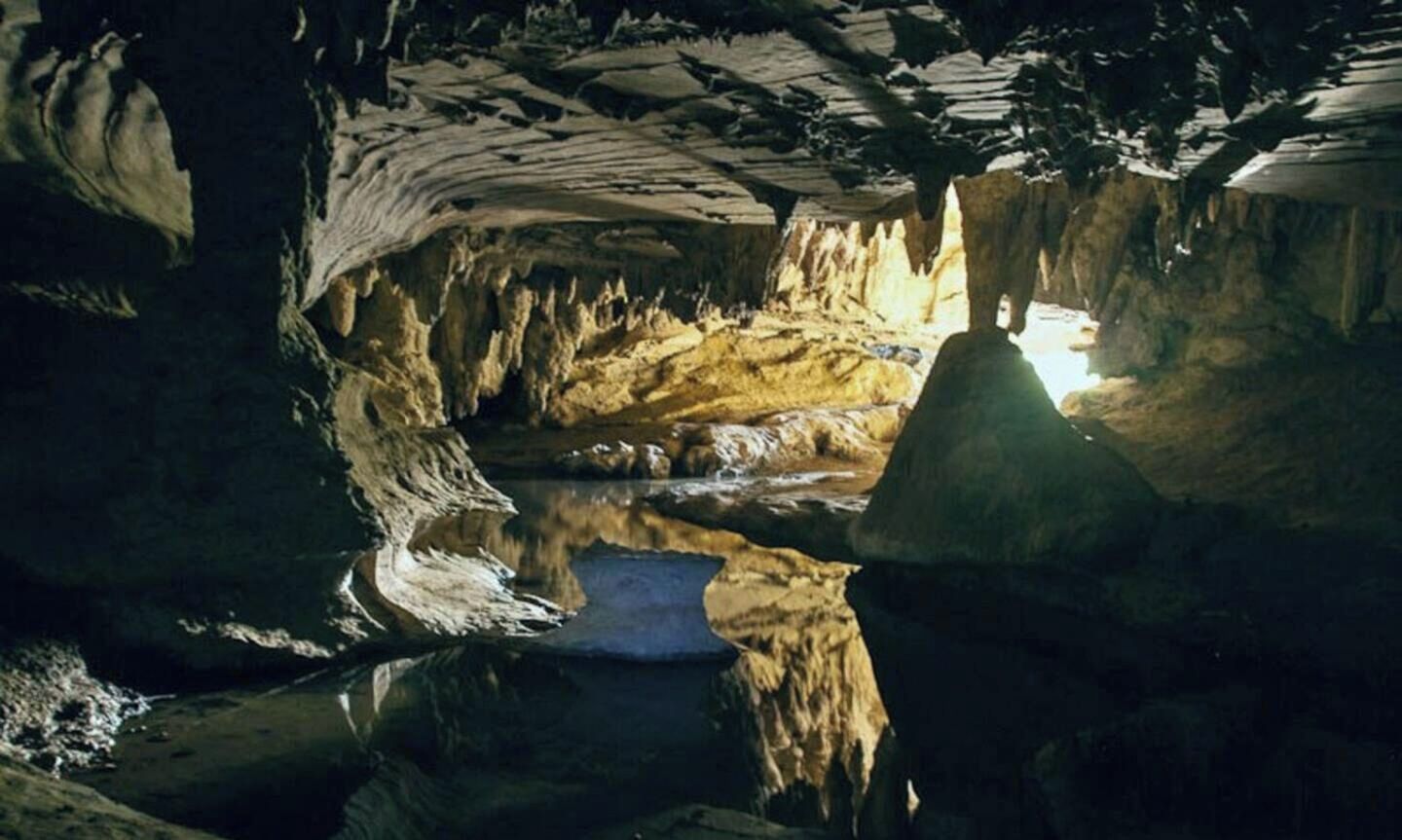 Cueva con estalactitas, un charco de agua y una abertura.