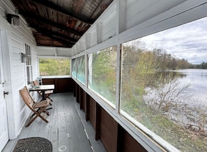 Eine überdachte Veranda mit Tisch und Stühlen, große Fenster mit Blick auf ein Gewässer.