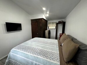 Ein Schlafzimmer mit Bett, Wandfernseher, Kleiderschrank und einem Fenster mit Vorhängen.