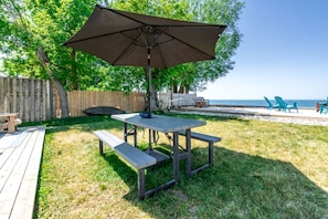A patio with a table and benches, a wooden deck, and a view of the beach. - Stunning Cottage with Nice Views and Fire Pit in Leamington, Ontario (Leamington)