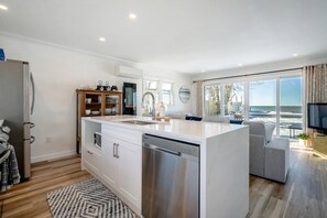 A modern kitchen with a central island, a built-in dishwasher, and a dining area with a view of the beach. - Stunning Cottage with Nice Views and Fire Pit in Leamington, Ontario (Leamington)