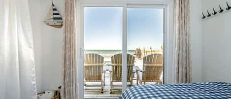 A bedroom with a large sliding glass door leading to a beach view, a checkered bedspread, and a wicker basket on the floor.